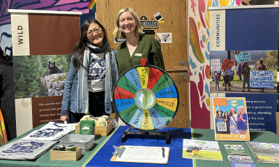 Two women standing at a booth with posters, flyers, and a prize wheel