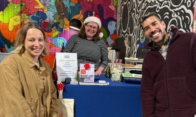 Three smiling people pose for the camera, in front of colorful, intricate murals