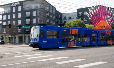 A blue lightrail train passes by colorful public sculptures and apartment buildings