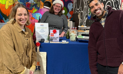 Three smiling people at an indoor market, next to a colorful mural