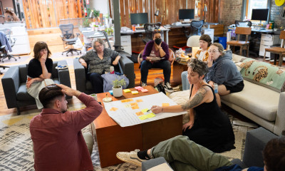 A group of people seated around a low coffee table in an office/living room setting