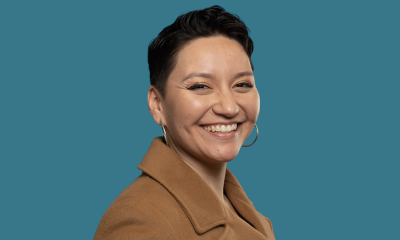 A smiling person with short, dark hair; hoop earrings, and a tan blazer