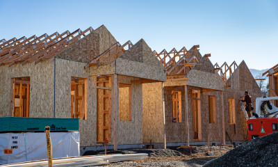 Middle housing being built (all plywood frames/walls) with a worker placing a panel on the farthest home (on the right).