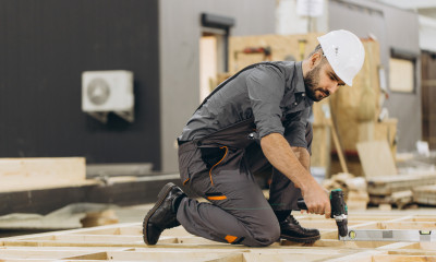 A man in a white hard hat uses a drill on some flooring
