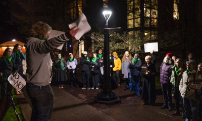 A woman raises her arms as she addresses a rally gathered outside in the dark