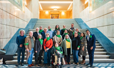 A smiling group of people wearing green bandanas in the state capitol