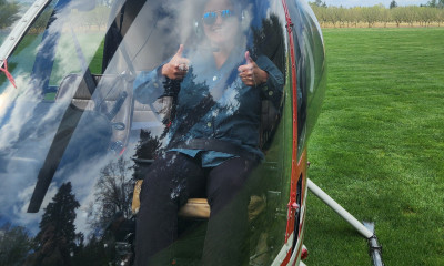 A smiling person giving a double thumbs up in a helicopter parked on a grassy field.