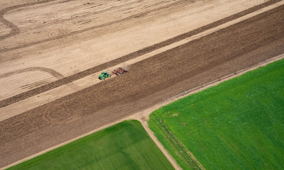 Aerial view of farm equipment in a brown-colored field, next to a vibrantly green field