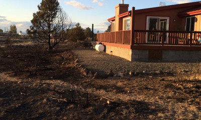 A home surrounded by burnt ground and burnt vegetation. The home itself looks untouched, and it has a border of gravel with no vegetation around it (defensible space).