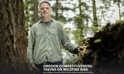 Screenshot of the header of an article, with the title, "Oregon Competitiveness: Taking on Wildfire Risk." This is layered over a photo of a man in a sage-green shirt standing in a dense forest.