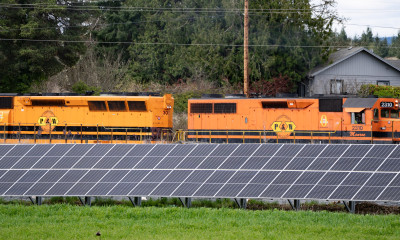 A small solar array alongside a train track, with an orange engine traveling along it