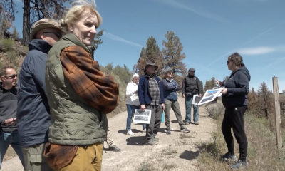 A group of people in an arid, outdoor setting, gathered around a person talking to the group.