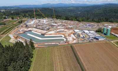 A landscape of forested areas and agricultural fields that is disrupted abruptly by a large scar from industrial construction.