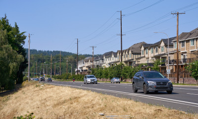 Cars traveling down a road that is parallel to a row of townhomes