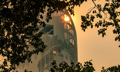 A tower with an image of a woman's face and trees on it is framed by tree branches. The sun is shining through a window at the top of the tower. The air is orange and hazy from wildfire smoke.