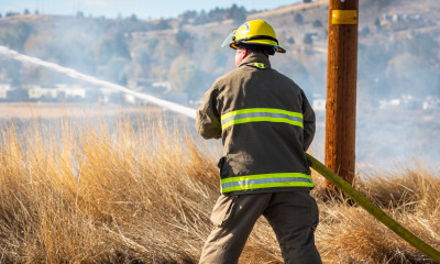 Back of a firefighter spraying a hose on a dry brown field