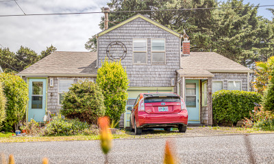 A duplex with weathered gray siding, pale blue doors, and a red car parked out front