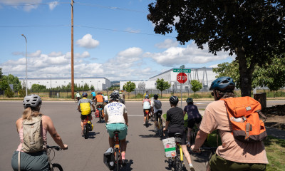 A group of people on bikes near white, windowless buildings (data centers)