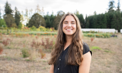 A smiling woman with long brown hair and a black shirt, in a rural setting