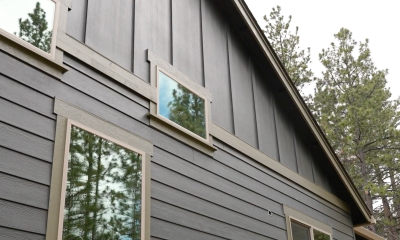 A home with gray siding, surrounded by Ponderosa pines which are also reflected in the windows